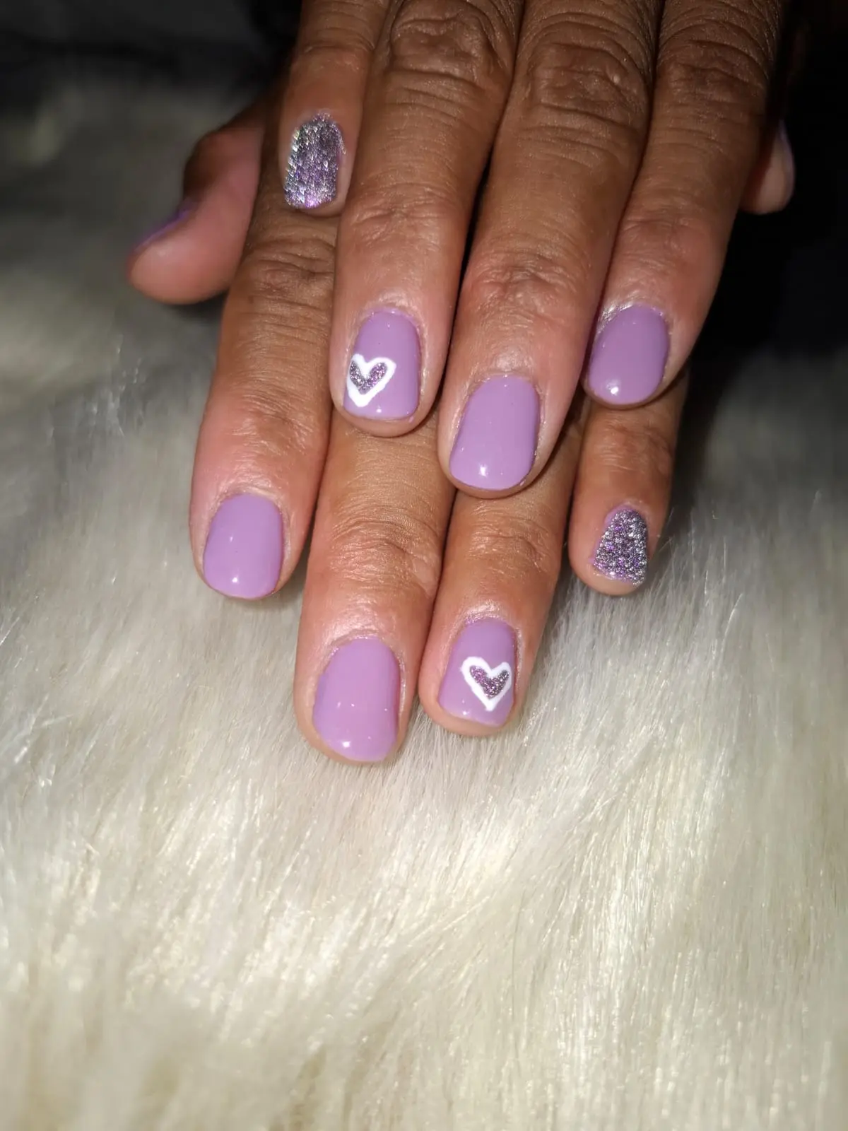 Diseño de uñas en color lila con un pequeño corazón blanco