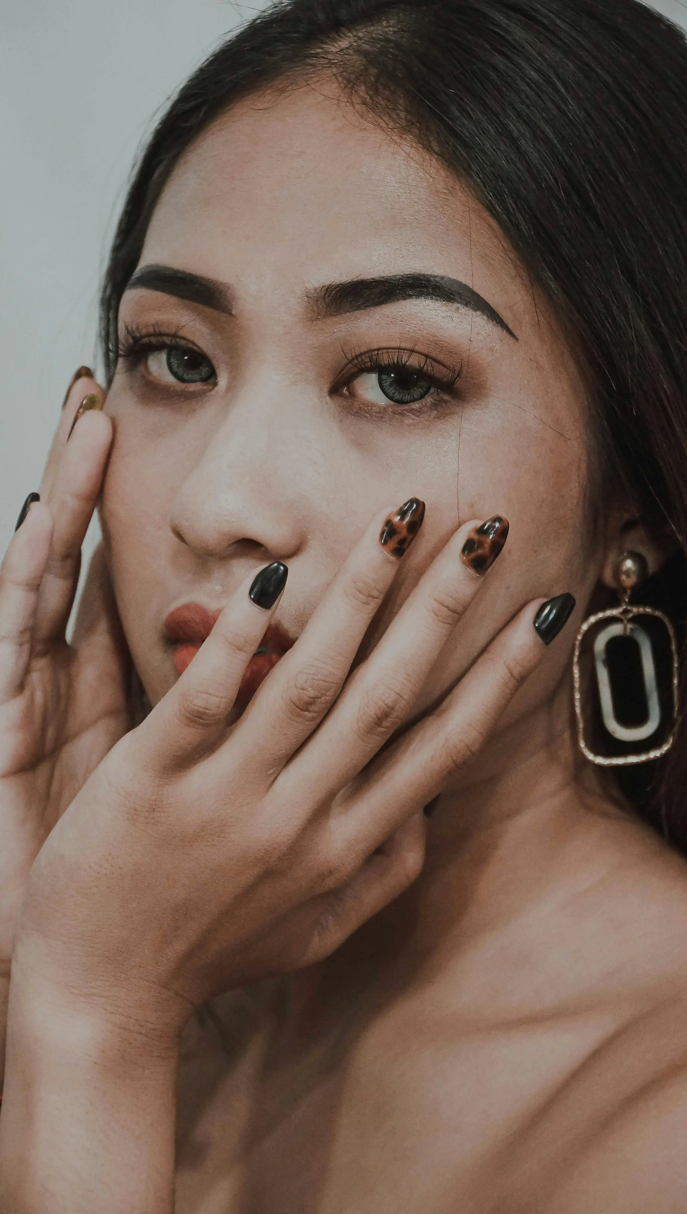 Mujer con uñas semipermanentes oscuras con diseño de leopardo.